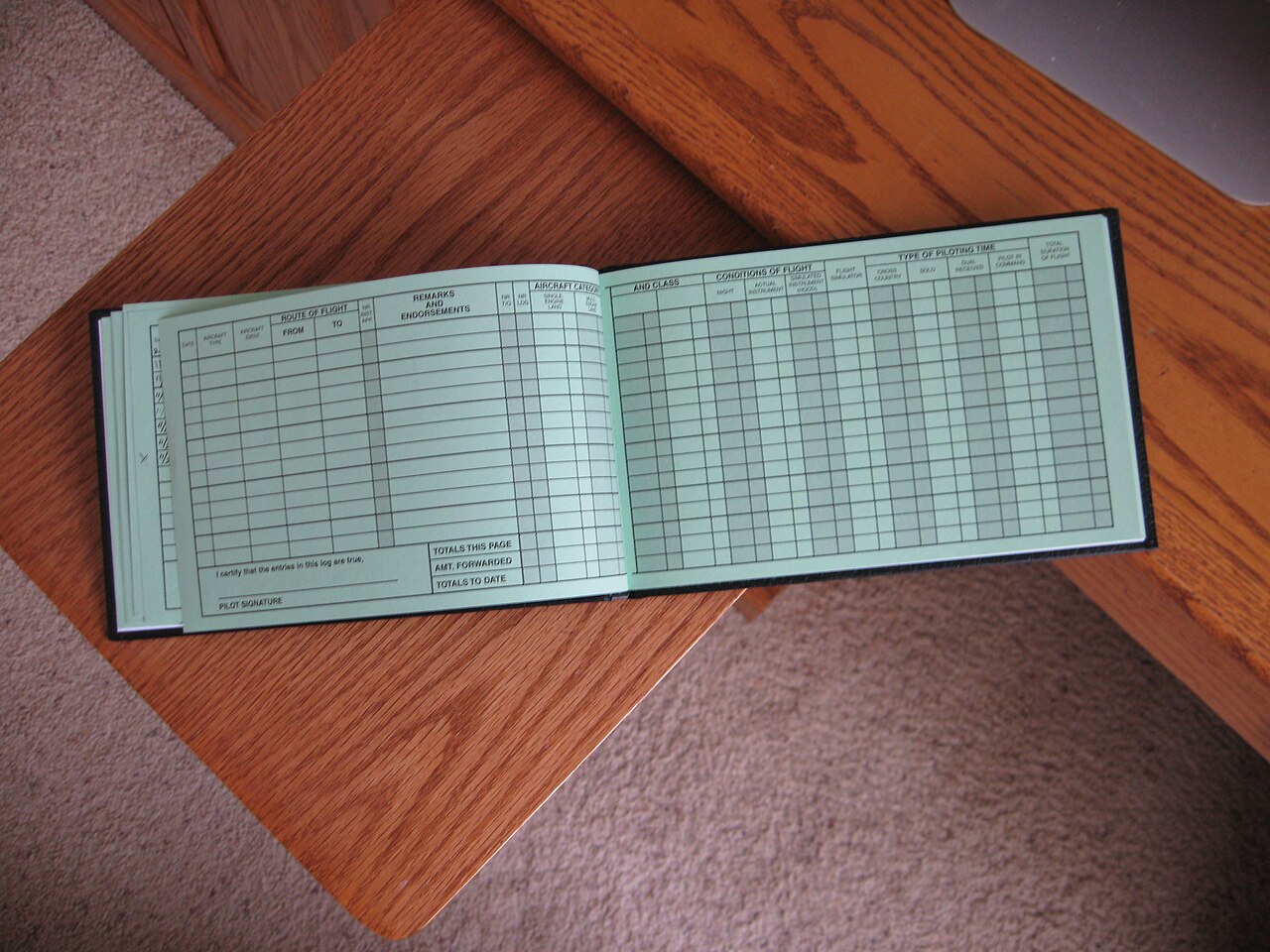 An open paper logbook with blank pale green pages and columns for date, aircraft and route